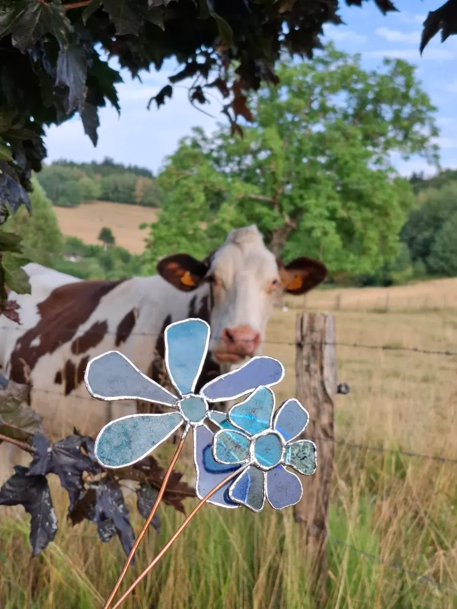 Fleurs décoratives en verre bleu au premier plan avec une vache dans un champ en fond.