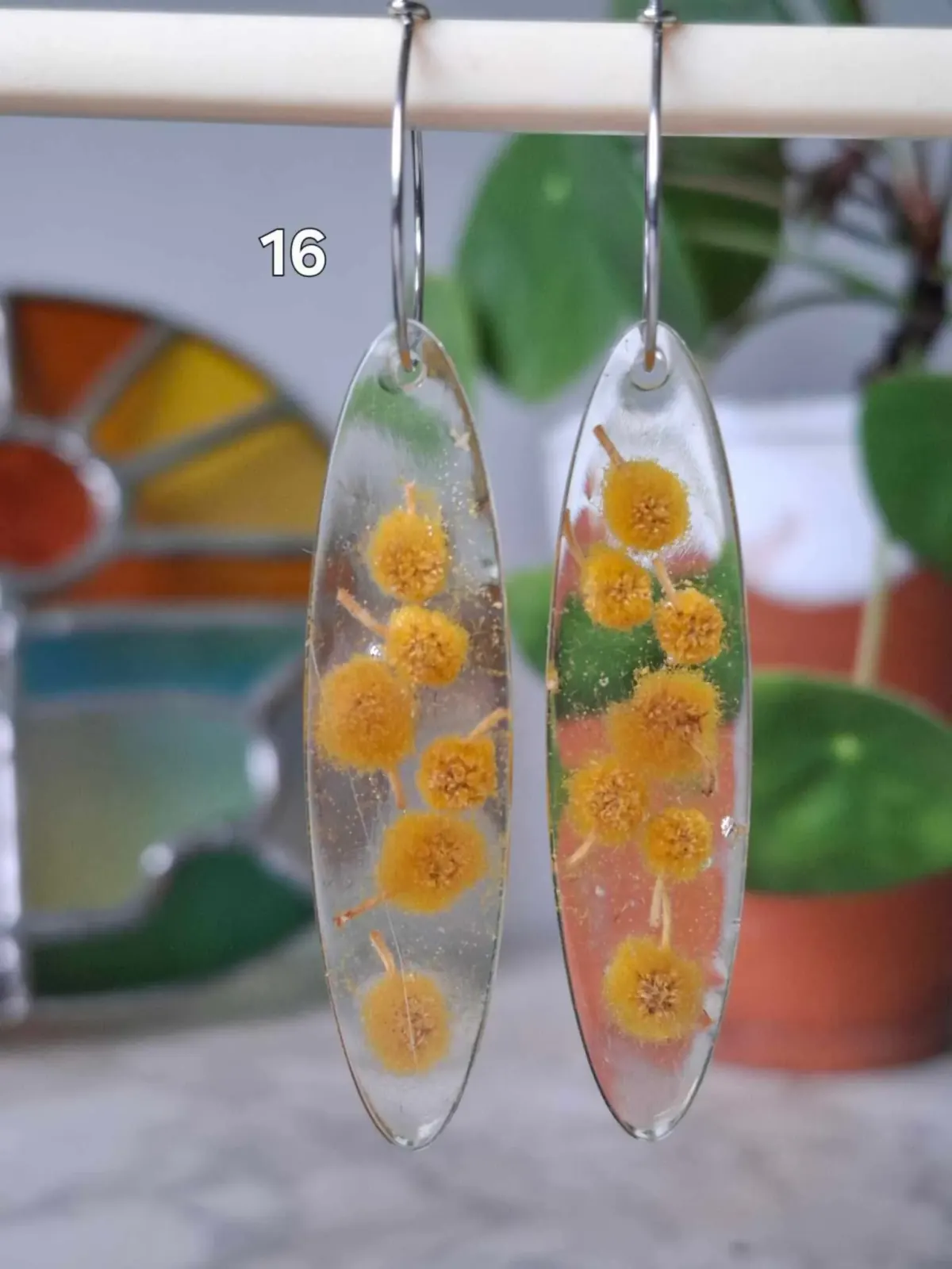 Boucles d'oreilles ovales transparentes en résine avec de petites fleurs jaunes séchées à l'intérieur.