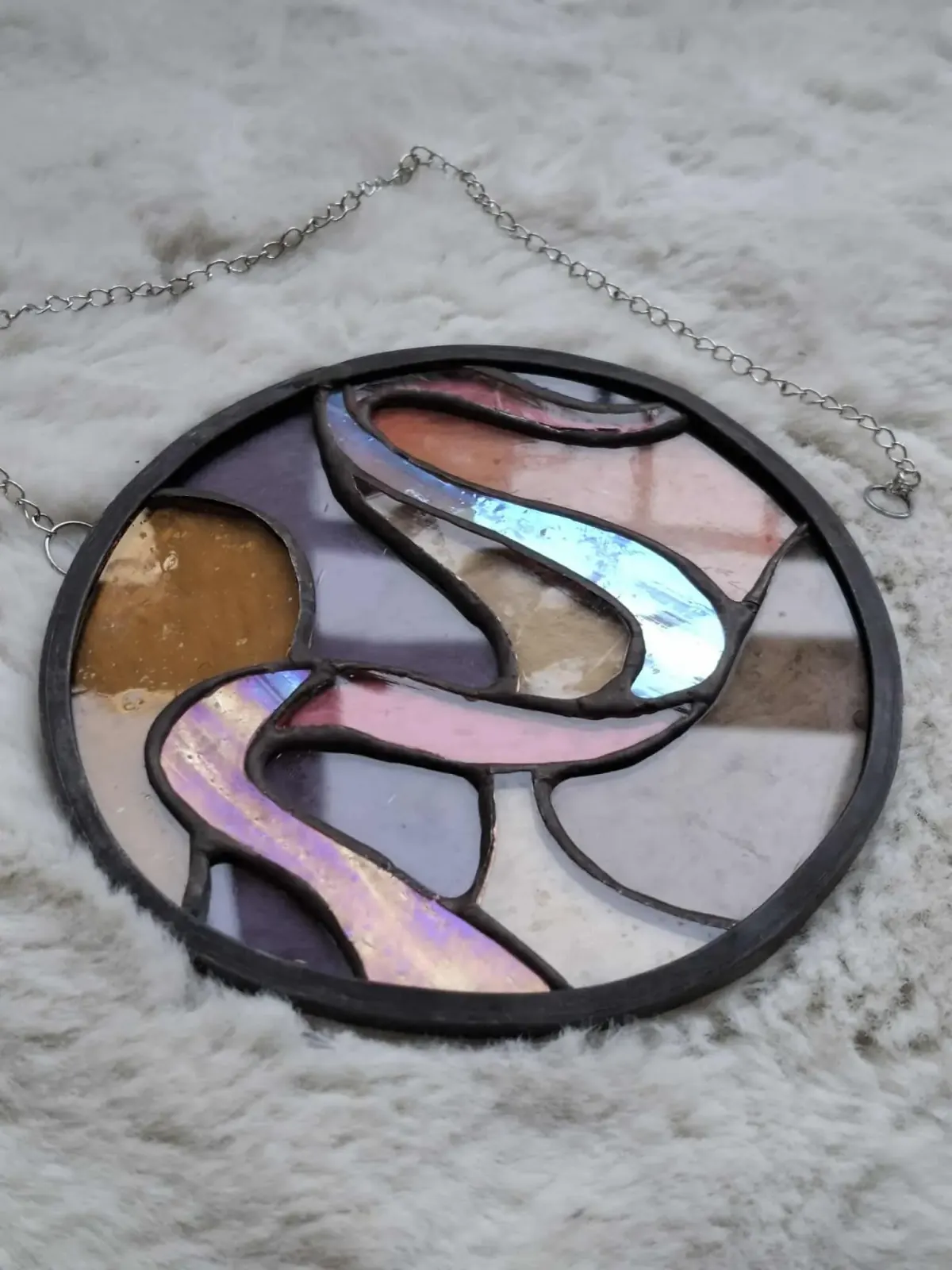 Vitrail rond aux motifs ondulés rose, violet et doré, posé sur une surface blanche texturée.