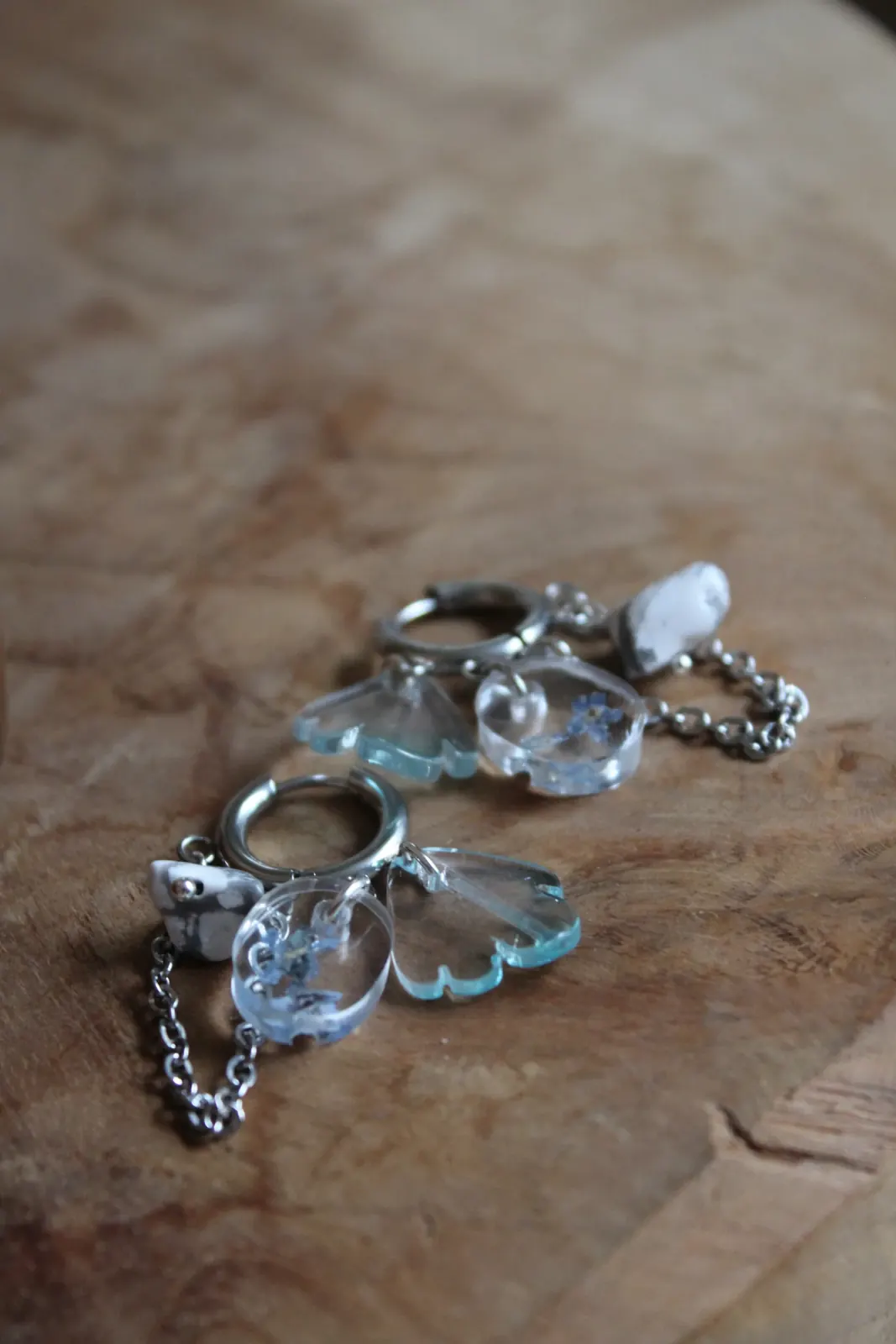 Paire de boucles d'oreilles créoles argentées avec pendentifs fleurs bleues et pierre blanche sur bois.