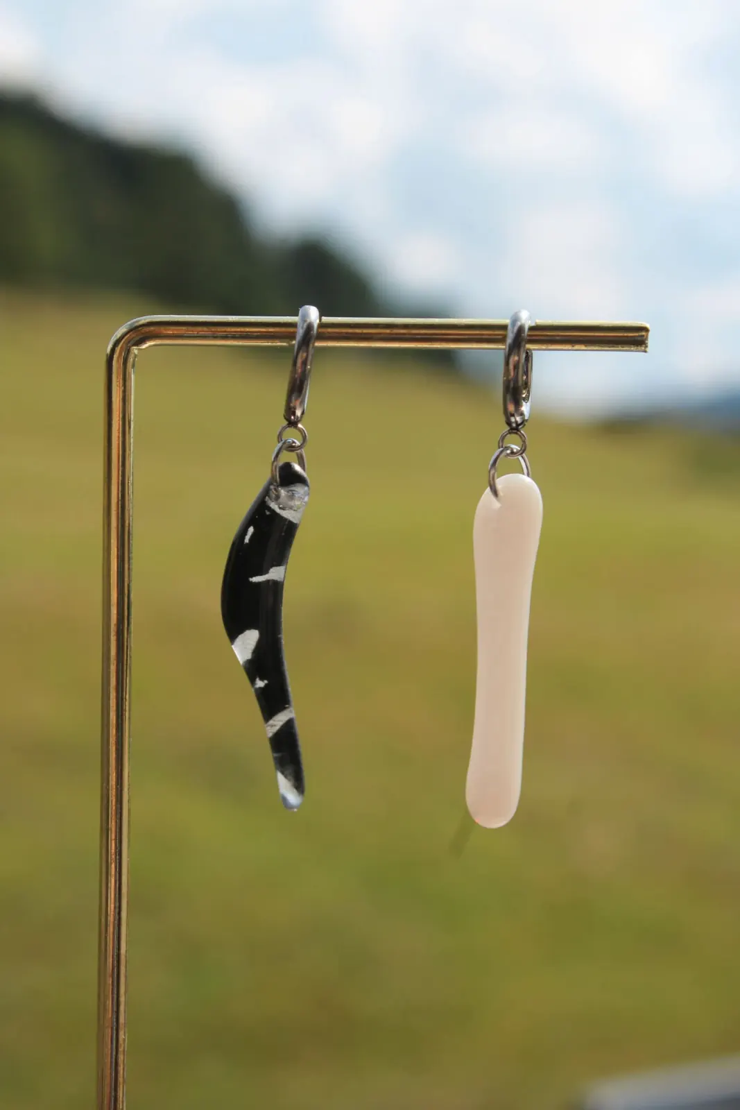 Boucles d'oreilles asymétriques, l'une noire courbée et l'autre blanche droite, suspendues sur un support doré.