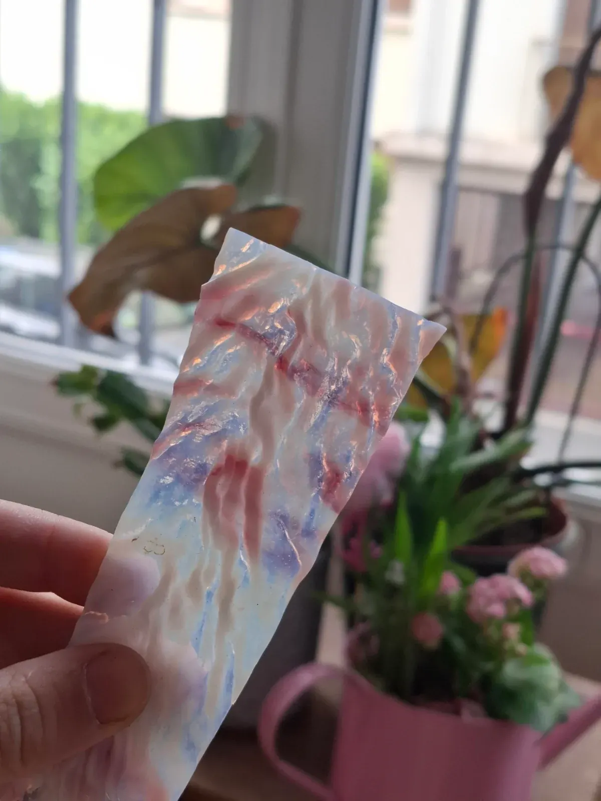 Pièce de verre rectangulaire et texturée aux nuances marbrées de blanc, rose et bleu tenue à la main.