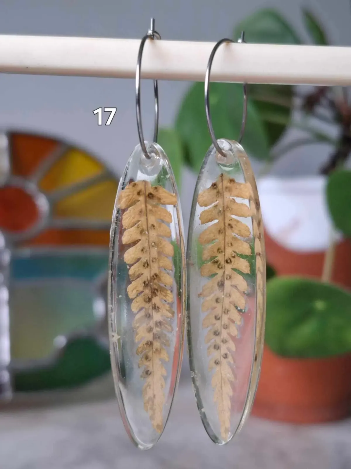 Boucles d'oreilles ovales transparentes en résine renfermant une feuille de fougère séchée marron clair.