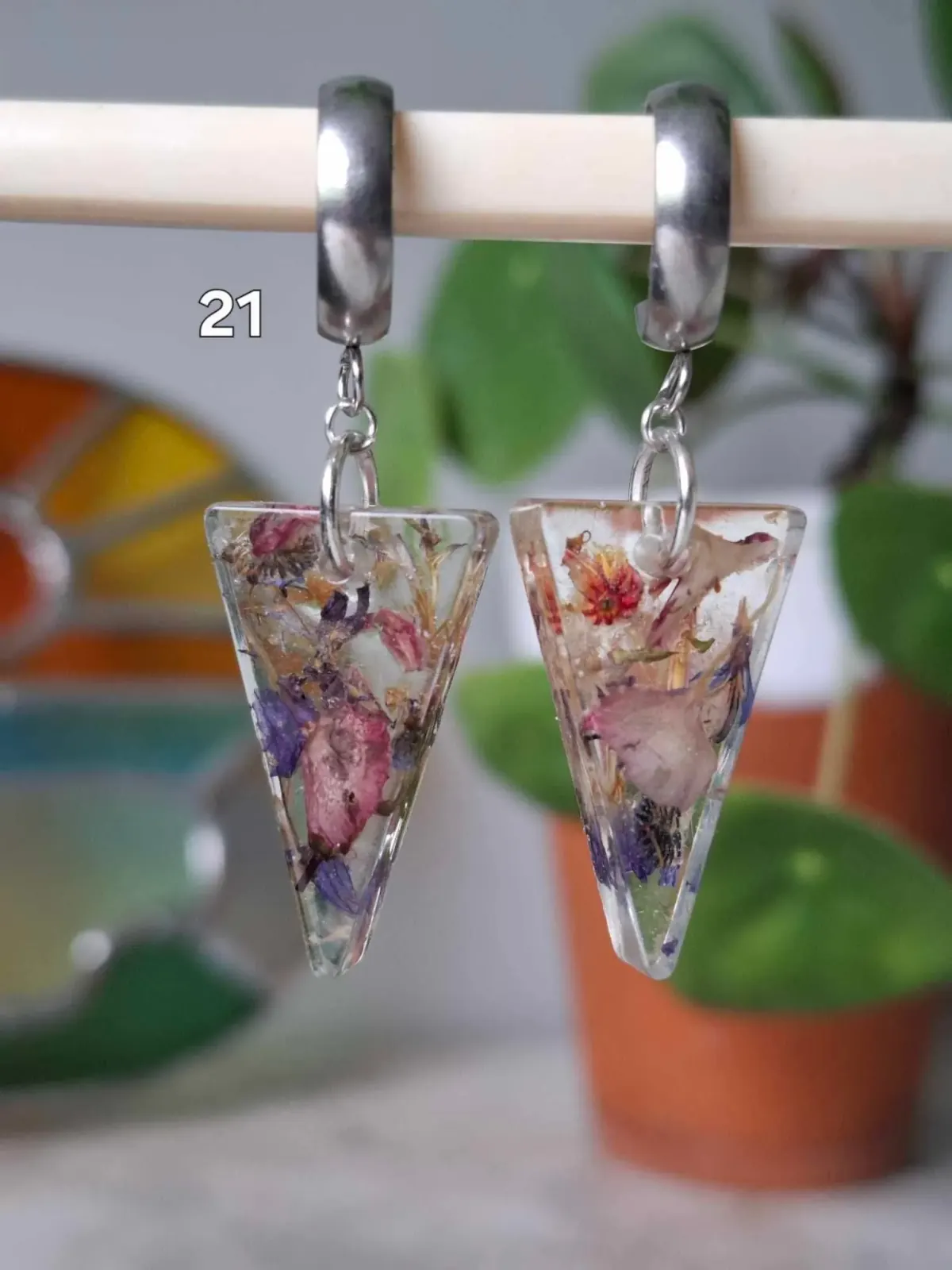 Boucles d'oreilles triangulaires en résine transparente avec de petites fleurs séchées colorées.