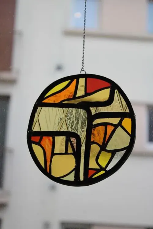Vitrail rond suspendu aux nuances de jaune, orange et rouge, avec des motifs abstraits géométriques.