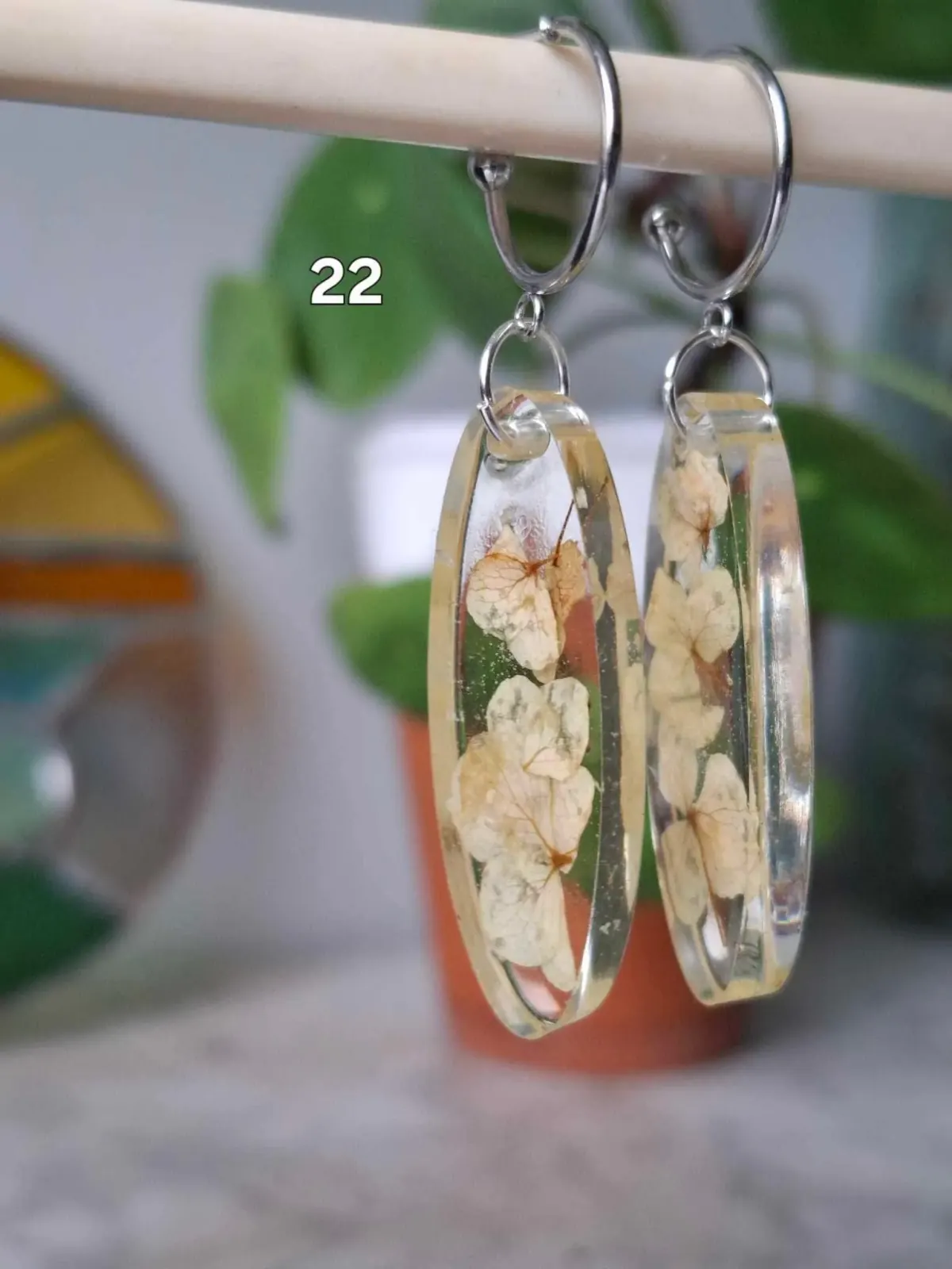 Boucles d'oreilles ovales transparentes en résine avec de petites fleurs séchées blanches suspendues.