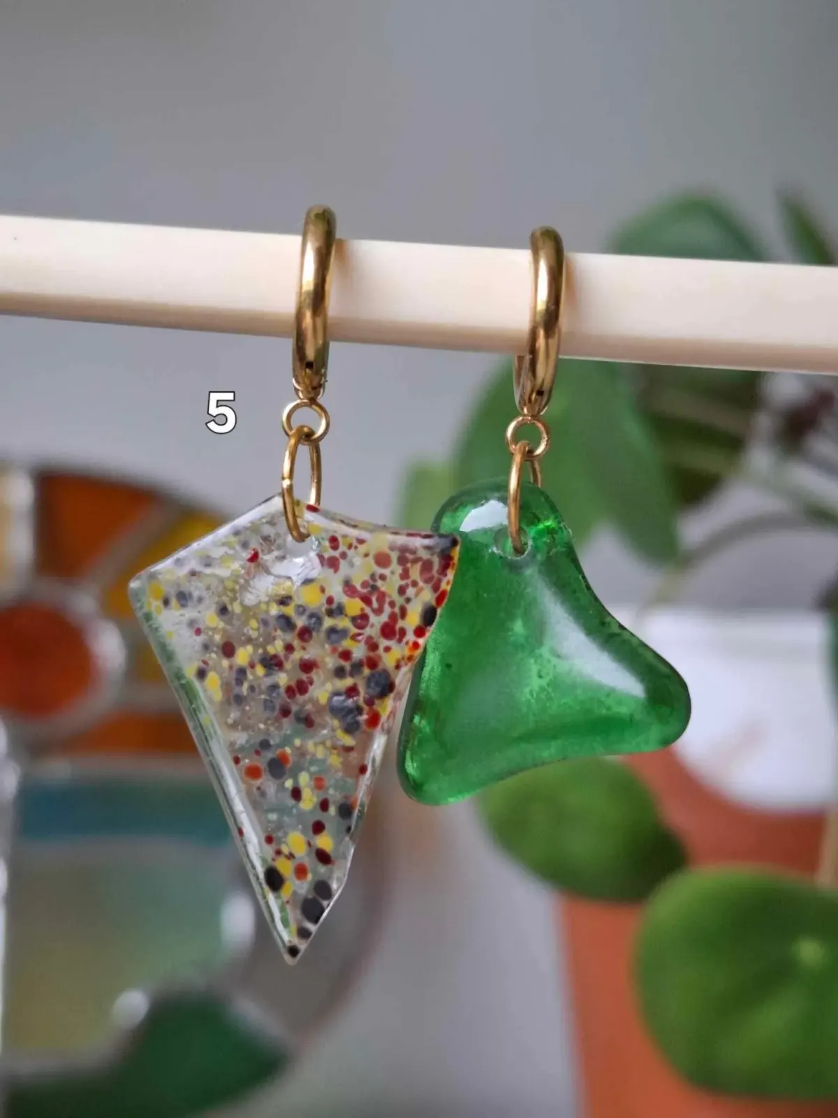 Boucles d'oreilles asymétriques : une triangulaire mouchetée multicolore et une verte en verre suspendues.