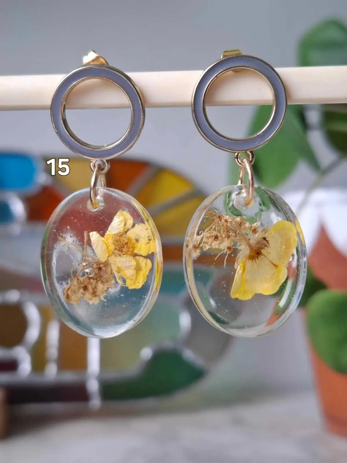 Boucles d'oreilles pendantes avec anneau métallique et médaillon ovale transparent contenant une fleur jaune.