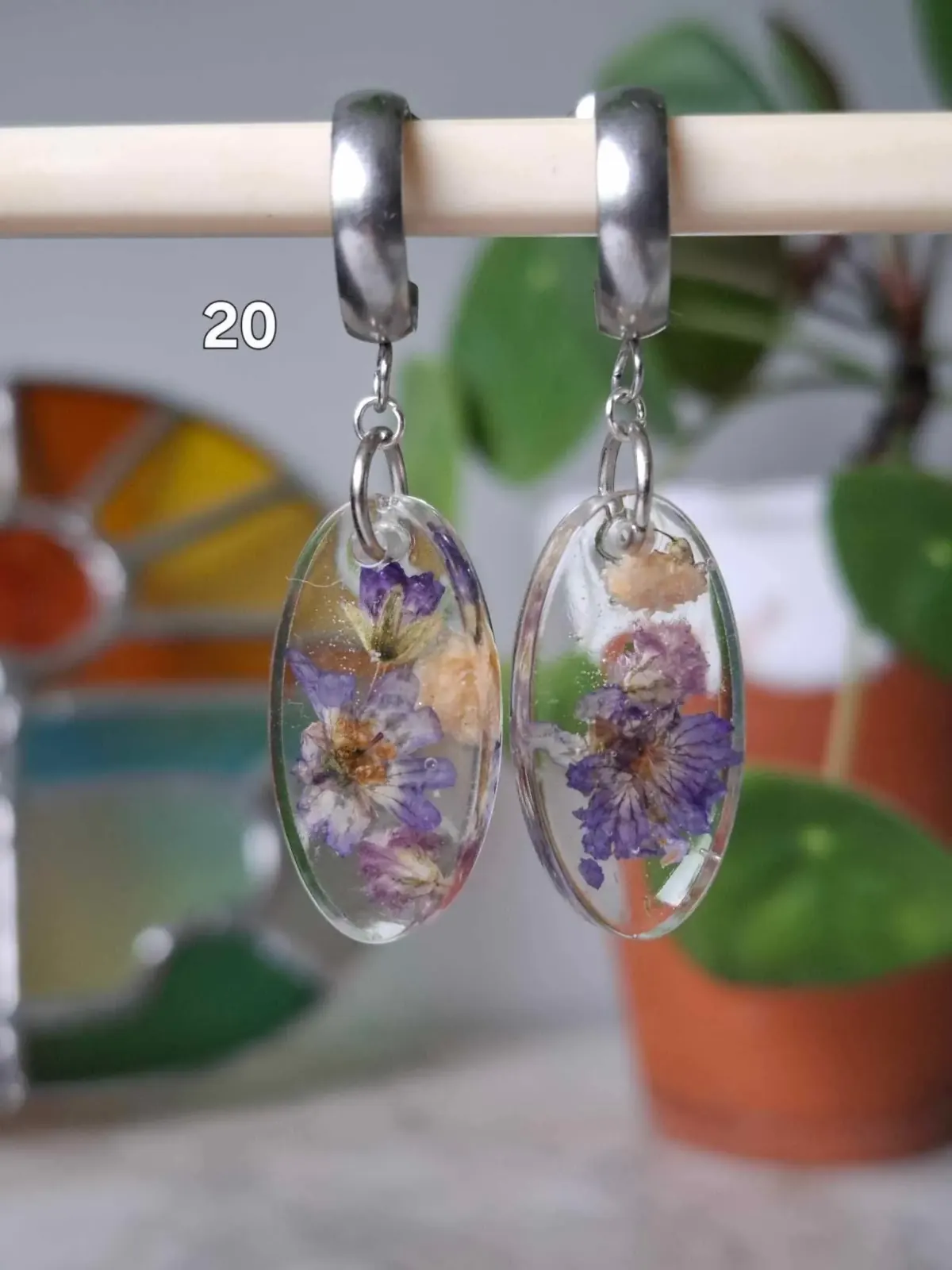 Boucles d'oreilles ovales transparentes en résine avec de petites fleurs violettes séchées suspendues.