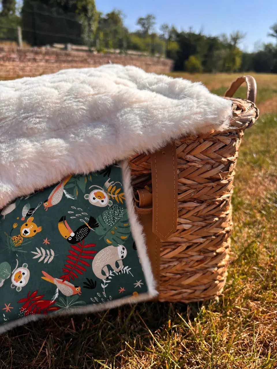 Couverture bébé double-face posée sur un panier en osier, côté polaire blanche et côté vert à motifs animaux.