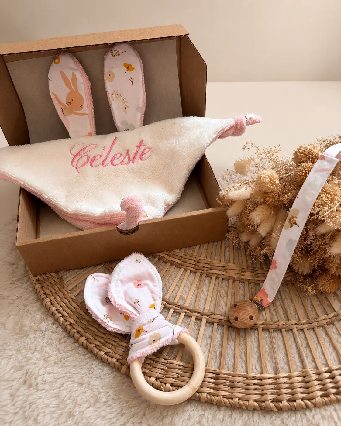 Coffret en carton ouvert dévoilant le doudou brodé Céleste, l'attache-tétine et l'anneau de dentition.