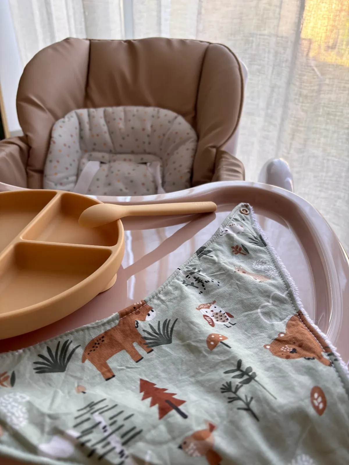 Bavoir bandana vert forêt posé à plat à côté d'une assiette et d'une cuillère pour bébé.