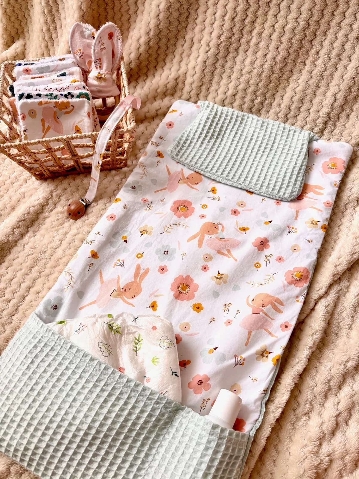 Tapis à langer déplié blanc à motifs de lapins roses et fleurs, avec poches en tissu nid d'abeille vert d'eau.