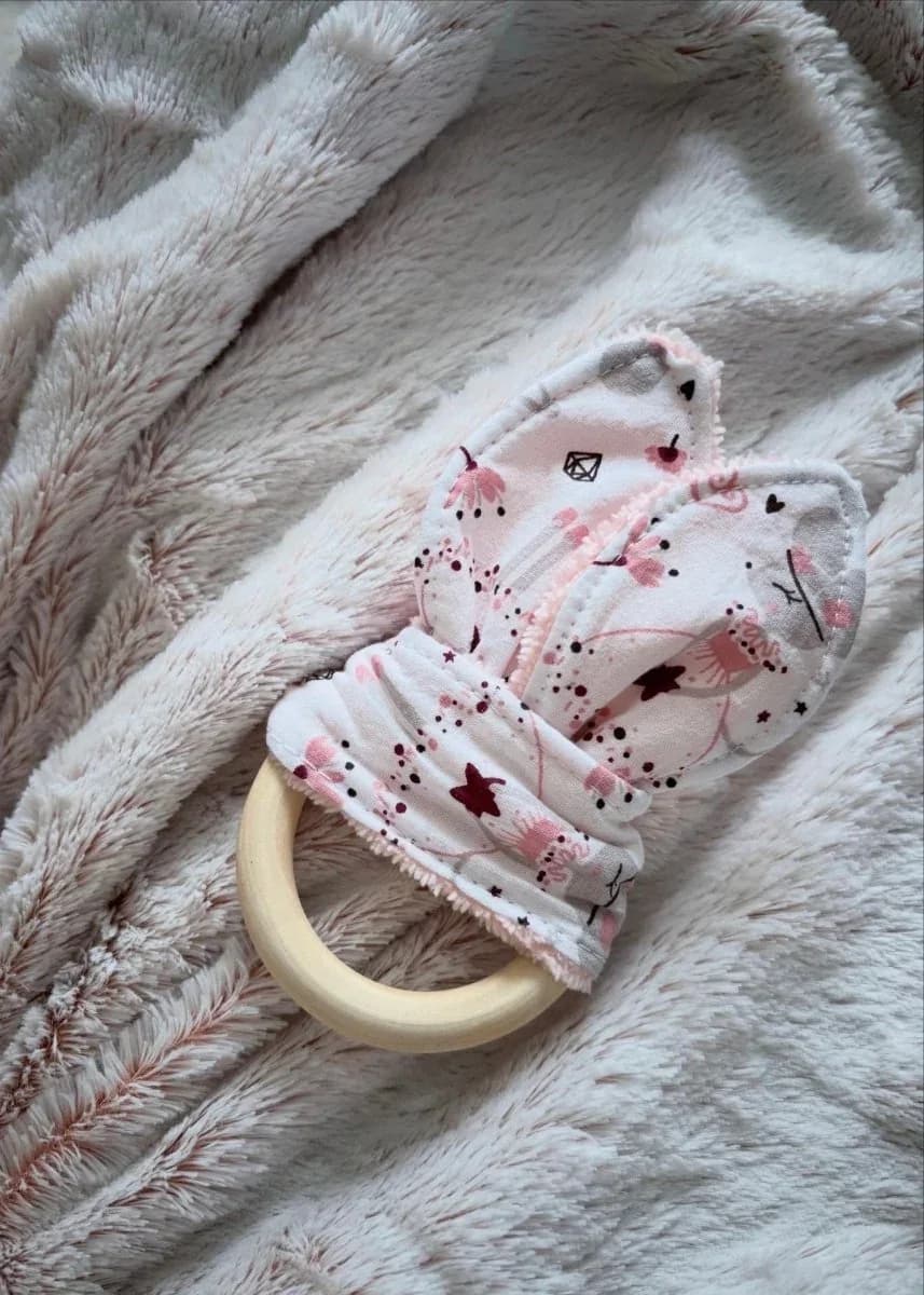 Anneau de dentition en bois avec tissu rose à motifs célestes posé sur une couverture douce.