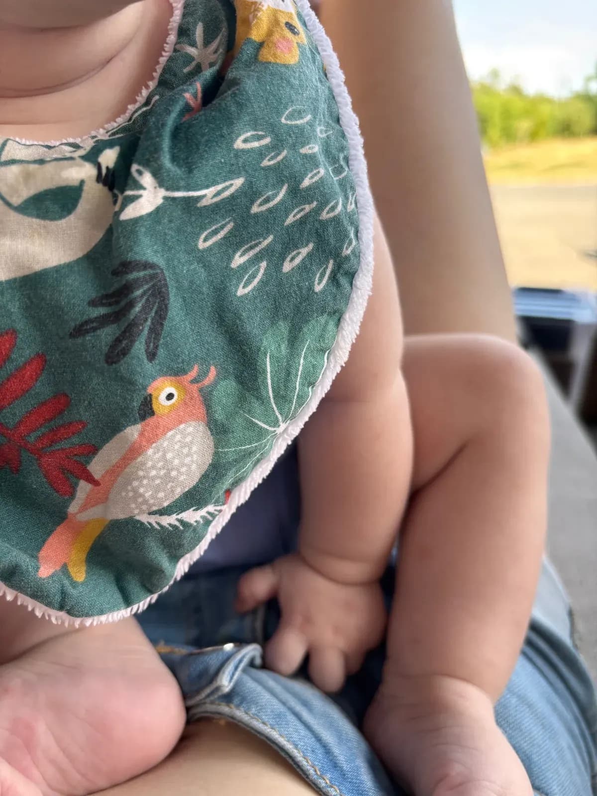 Gros plan d'un bébé portant le bavoir bandana vert imprimé d'un oiseau coloré et de feuillages.