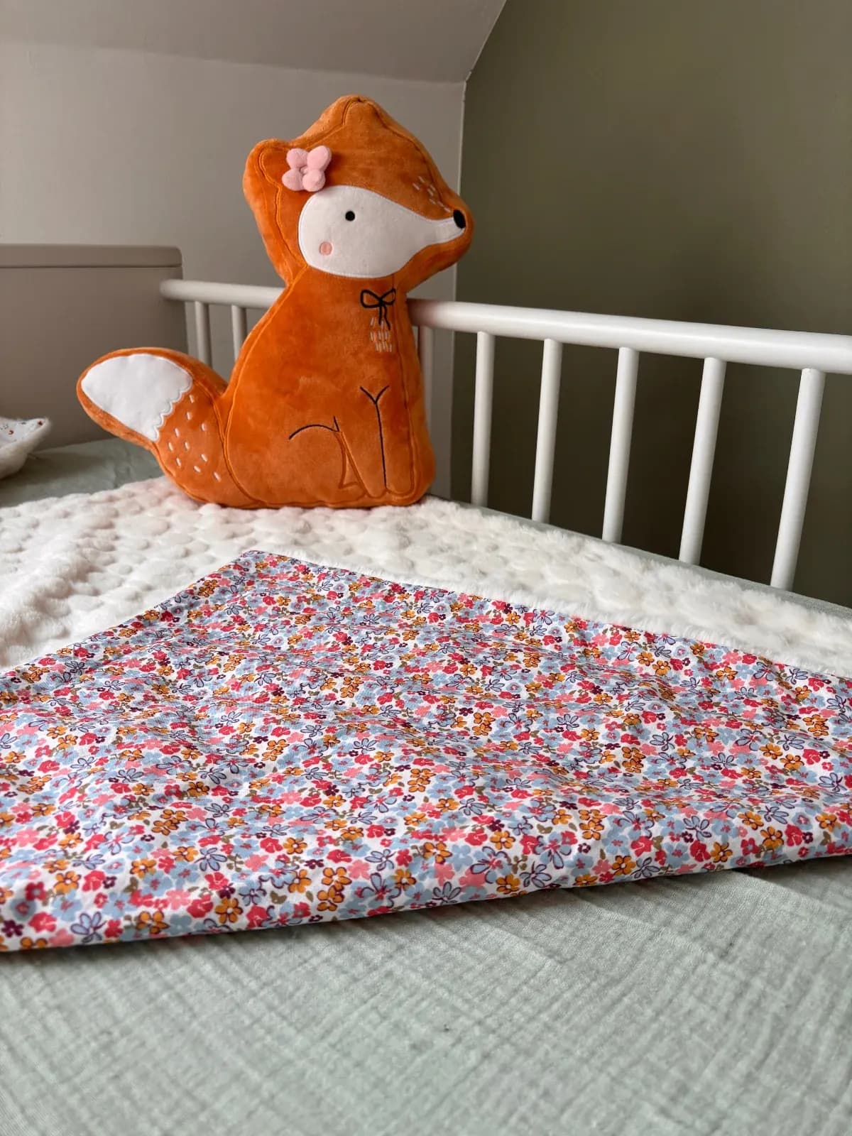 Couverture pour bébé à motifs de fleurs colorées posée près d'une peluche de renard orange.