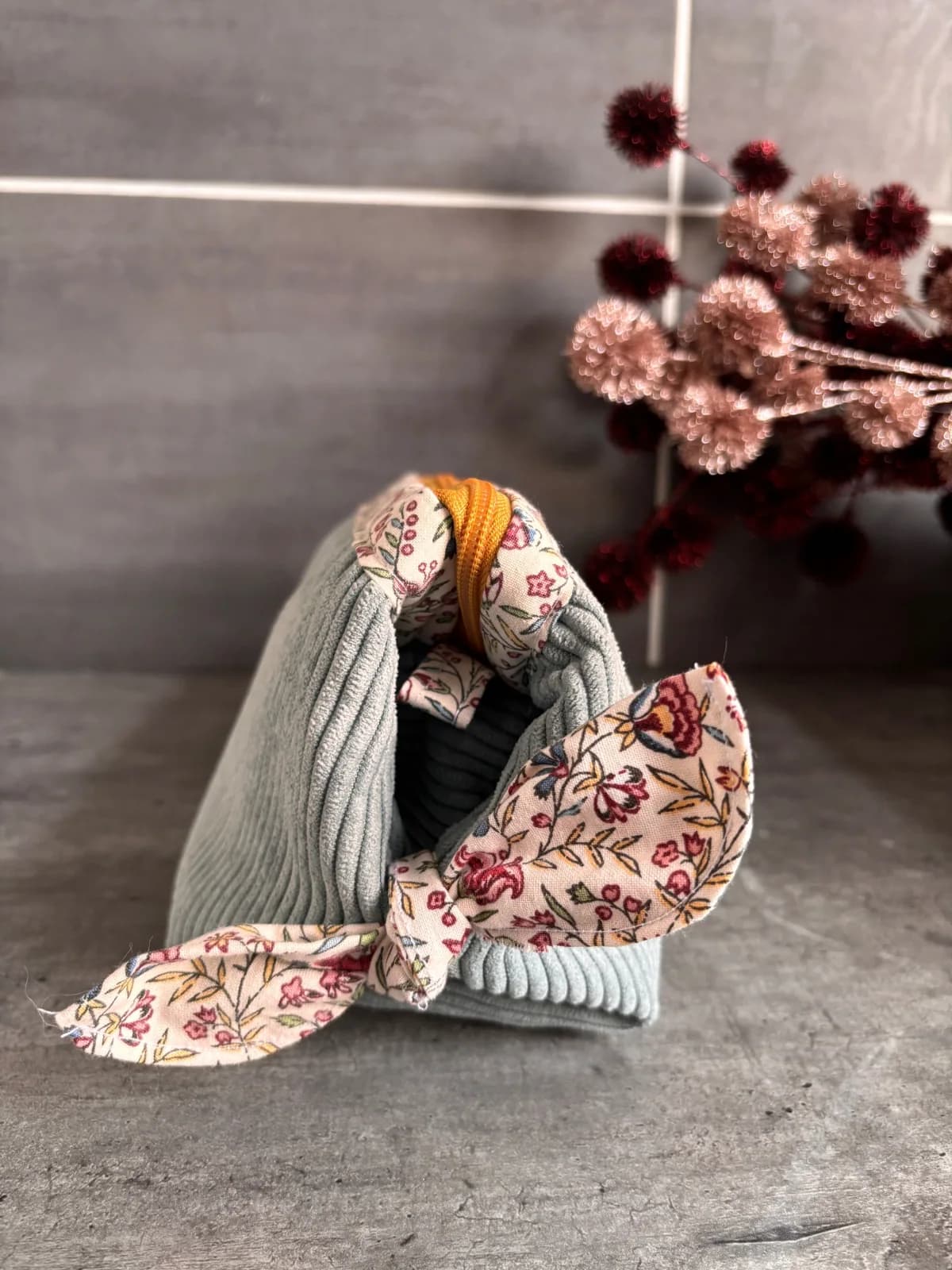 Trousse en velours côtelé vert d'eau fermée avec un nœud en tissu fleuri sur le côté.
