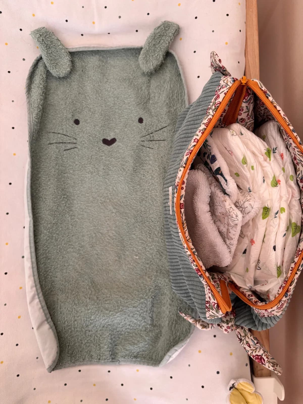 Vue de dessus de la trousse ouverte remplie de couches, posée à côté d'un tapis à oreilles de lapin.
