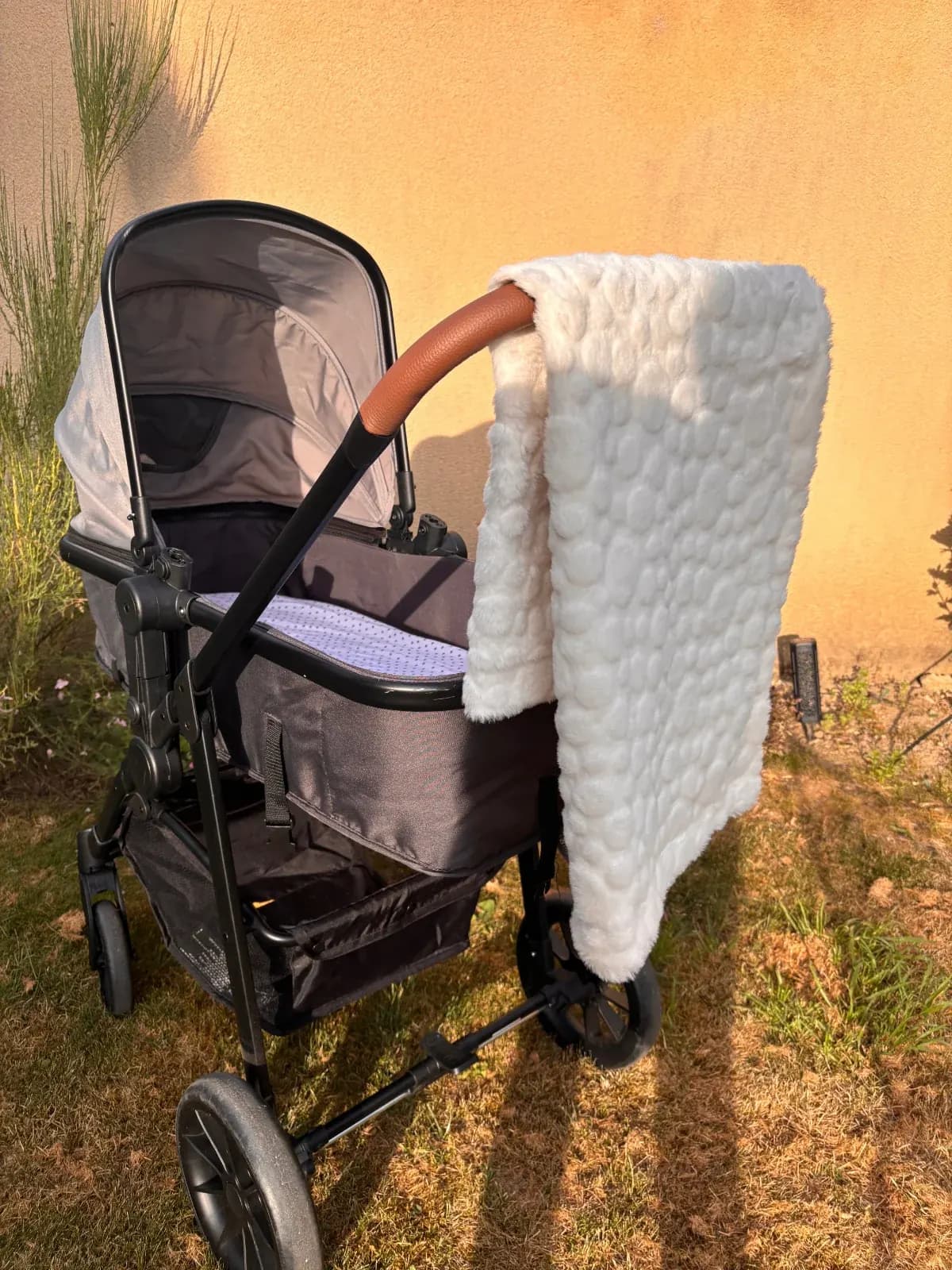 Couverture blanche texturée et moelleuse suspendue sur la poignée d'une poussette en extérieur.