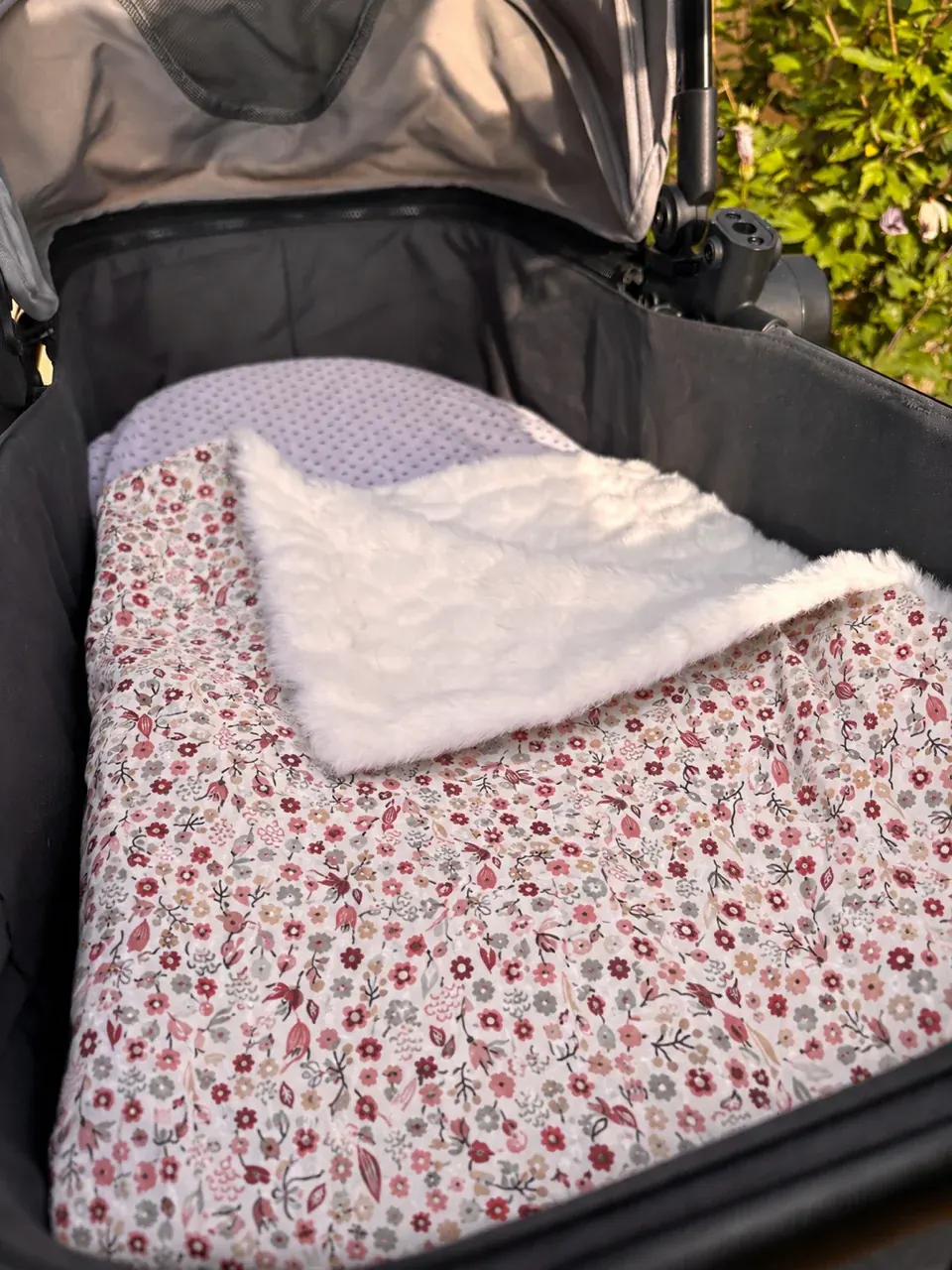 Couverture pour bébé à motifs floraux roses et revers blanc moelleux, disposée dans une poussette.