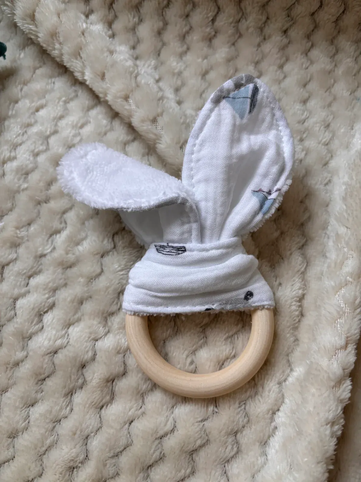 Anneau de dentition en bois avec oreilles en tissu blanc imprimé de petits bateaux bleus et gris.