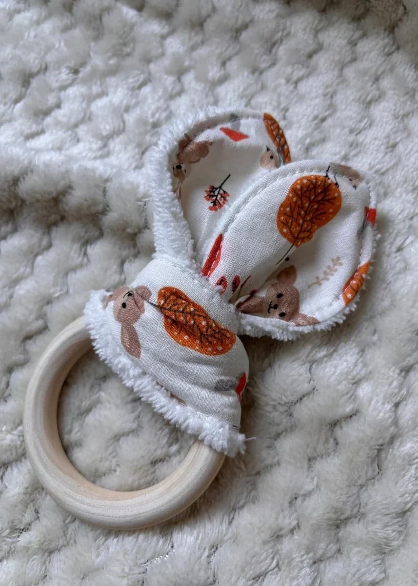 Anneau de dentition en bois avec tissu à motifs de feuilles d'automne et d'oursons sur un plaid blanc.