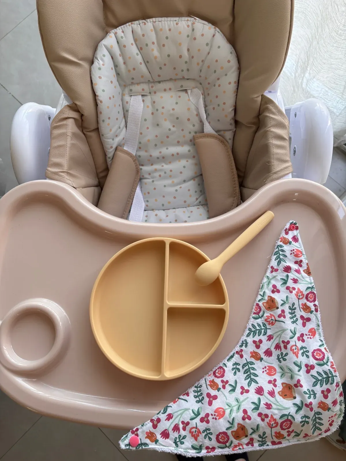 Vue d'ensemble d'une chaise haute avec une assiette jaune, une cuillère et le bavoir bandana fleuri.