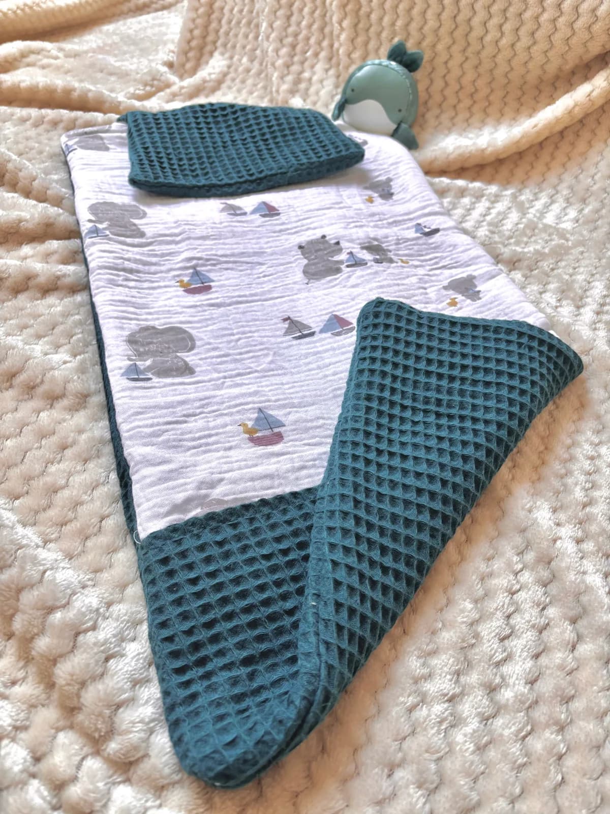 Tapis à langer déplié avec doublure en tissu nid d'abeille bleu canard, posé sur un plaid beige.