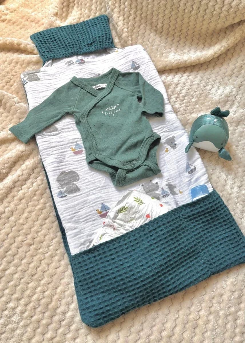 Tapis à langer blanc à motifs d'oursons et bateaux, avec un body vert et une peluche baleine.