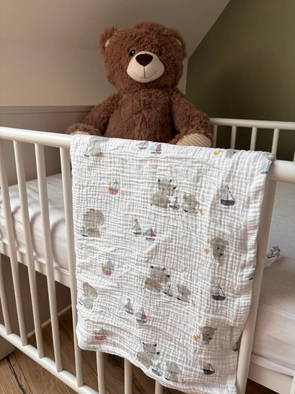 Lange blanc en gaze de coton à motifs d'oursons et bateaux, posé sur un lit de bébé avec un ours en peluche.