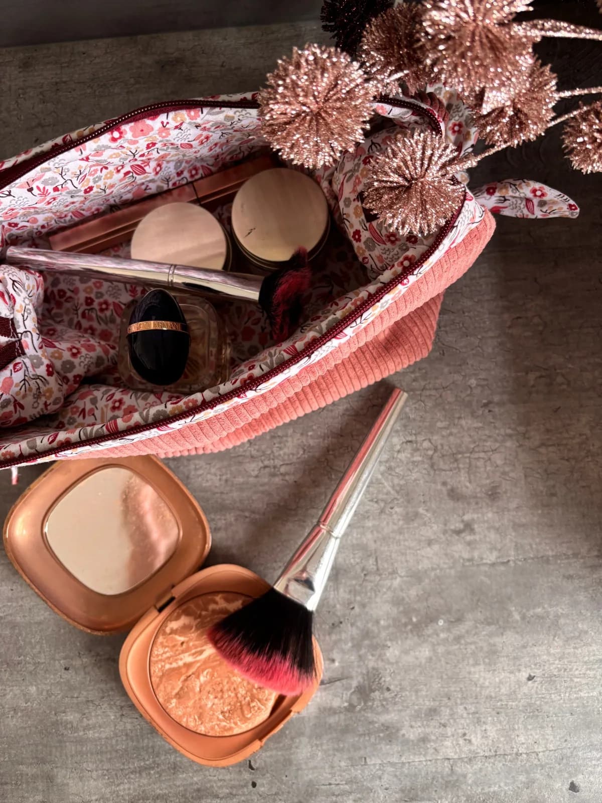 Gros plan d'une trousse en velours côtelé rose entrouverte sur un plaid blanc texturé.