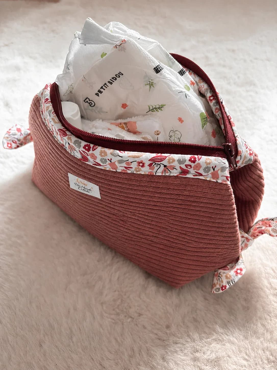 Vue du dessus d'une trousse ouverte contenant du maquillage et un parfum, posée sur un fond gris.