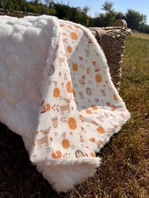 Couverture aux motifs de la forêt étalée sur un lit de bébé, à côté d'un grand coussin renard orange.