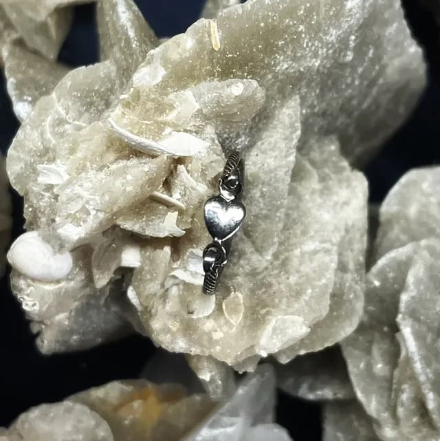 Bague fine en argent avec un motif de cœur, portée sur une phalange devant des cristaux beiges.