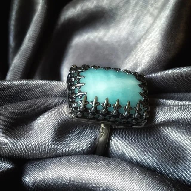 Bague en argent avec une calcite bleue rectangulaire posée sur un tissu satiné gris.