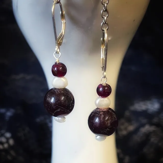 Gros plan de boucles d'oreilles dormeuses avec perles de grenat rouge foncé et perles d'eau douce blanches.