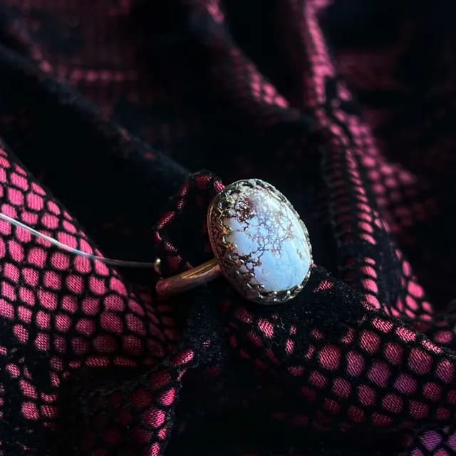 Bague en magnétite et argent avec pierre ovale blanche veinée de marron sur tissu dentelle noir et rose.