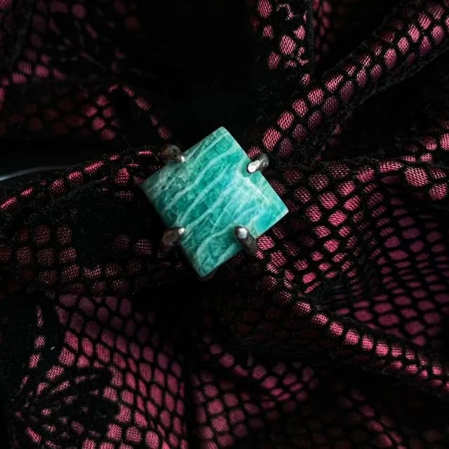 Gros plan d'une bague en argent sertie d'une amazonite carrée turquoise sur un tissu en dentelle rose et noir.
