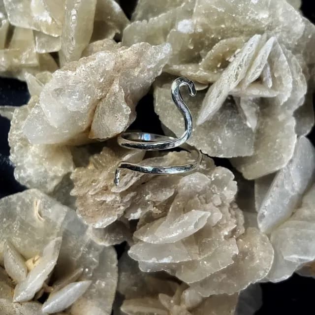 Bague de phalange en argent 925 en forme de serpent, posée sur des cristaux de rose des sables.