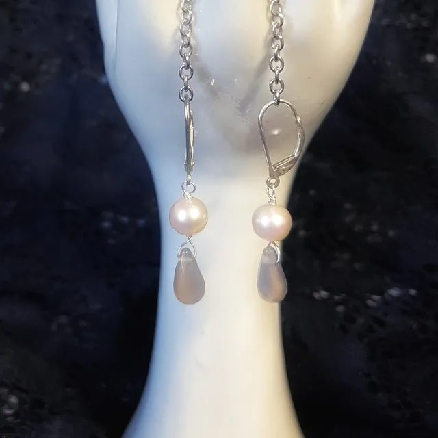 Boucles d'oreilles dormeuses en argent avec perle blanche et agate grise en goutte sur un support main blanc.