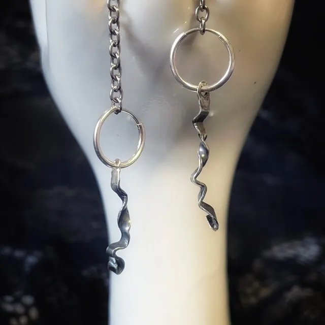 Créoles en argent avec pendants tordus et ondulés, suspendues sur un support blanc.