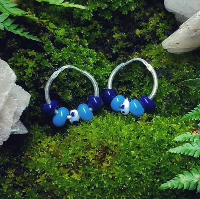 Créoles en argent ornées de perles de verre bleues et blanches, posées sur de la mousse verte.