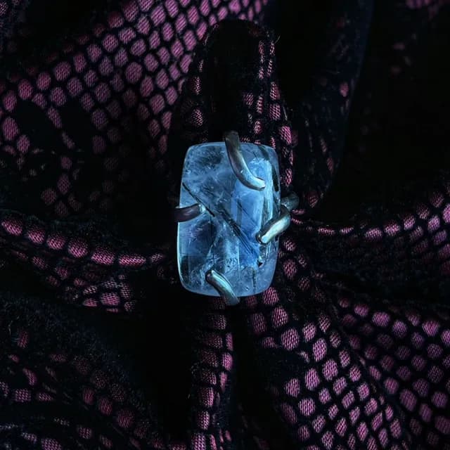 Bague en argent avec un quartz rectangulaire transparent à inclusions noires, posée sur un tissu alvéolé rose.
