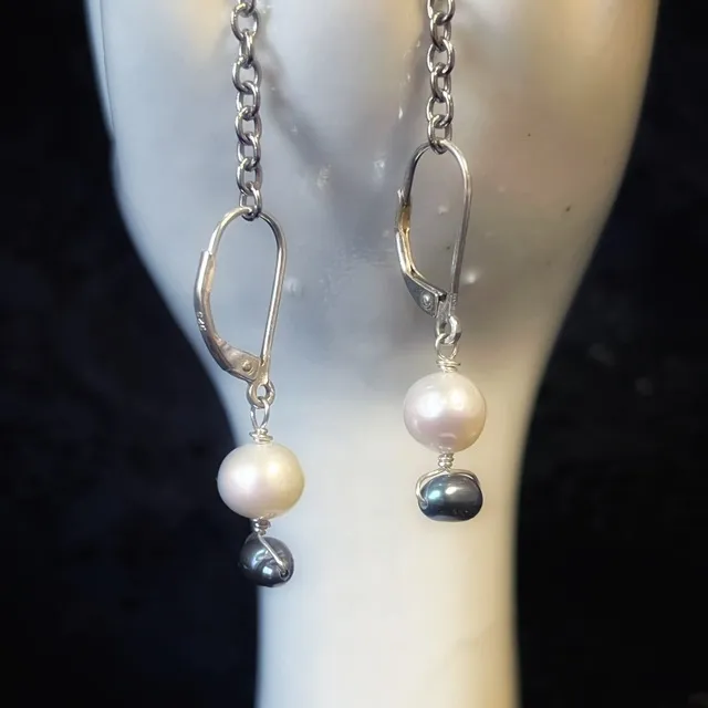 Gros plan de boucles d'oreilles dormeuses argentées avec perles blanches et grises sur présentoir main.