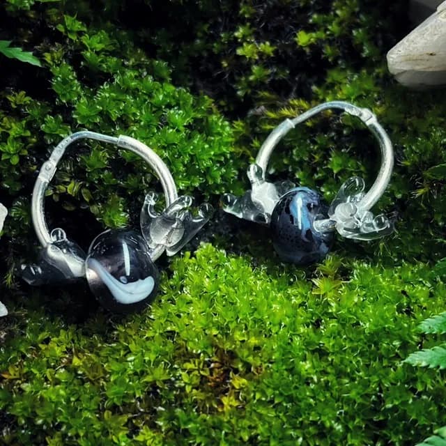 Créoles en argent avec perles de verre sombres aux reflets bleus et blancs, posées sur de la mousse verte.