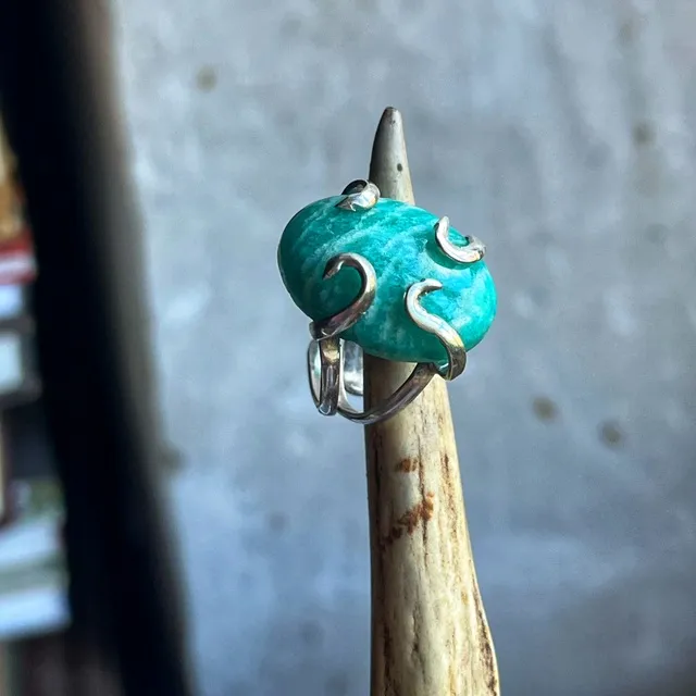 Bague en argent sertie d'une amazonite turquoise ovale, présentée sur un support en corne.