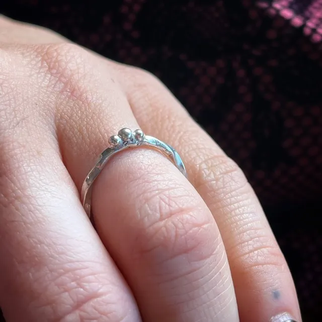 Fine bague en argent torsadée avec trois petites billes, portée au doigt.