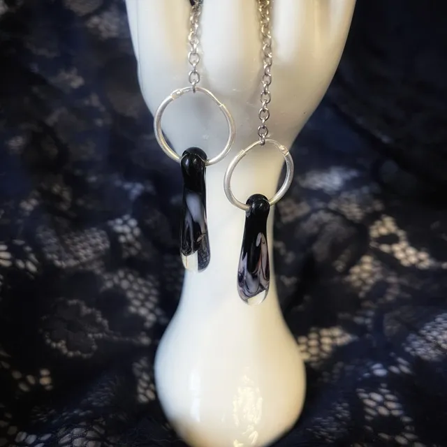Boucles d'oreilles créoles avec gouttes en verre noir et blanc suspendues sur un présentoir en forme de main.