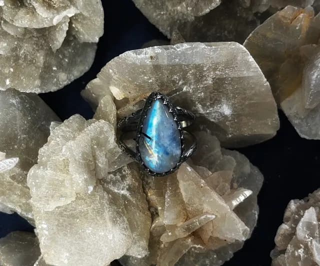 Bague en argent ornée d'une pierre de lune en forme de goutte, posée sur des cristaux bruts.