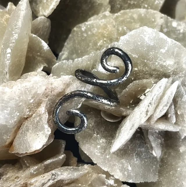 Bague de phalange argentée à double spirale texturée, posée sur des cristaux minéraux beiges.